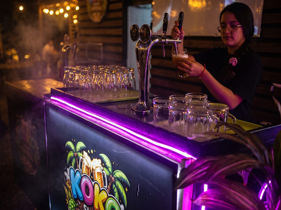 Barra de Koko Shop: una mesera sirve un schop de la schopera entre luces neón moradas y el logo iluminado